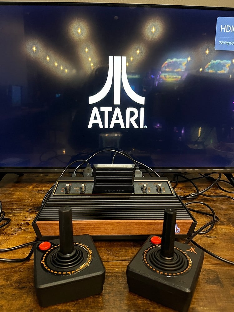 An Atari 2600 with two joysticks in front of a screen showing the Atari logo